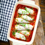 Overhead baked chorizo and brown rice stuffed squid in tomato sauce in a baking dish.