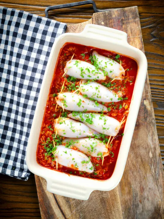 Overhead baked chorizo and brown rice stuffed squid in tomato sauce in a baking dish.