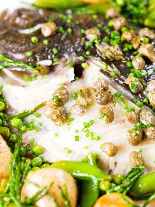 Overhead close-up whole roast turbot with capers, new potatoes and summer greens.