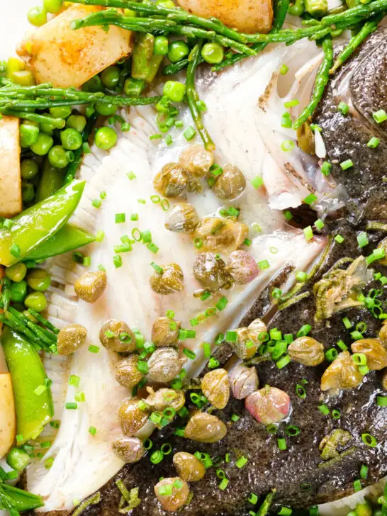 Overhead close-up whole roast turbot with capers, new potatoes and summer greens.