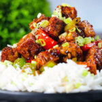 Close-up vegan/vegetarian Szechuan tofu with peppers and red onion served with white rice.