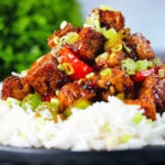 Close-up vegan/vegetarian Szechuan tofu with peppers and red onion served with white rice.