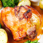 Close up baked apple and bacon stuffed pork chops, with cider gravy, potatoes and broccoli.