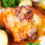 Close up baked apple and bacon stuffed pork chops, with cider gravy, potatoes and broccoli.