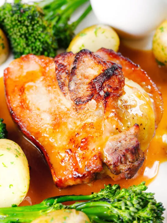 Close up baked apple and bacon stuffed pork chops, with cider gravy, potatoes and broccoli.