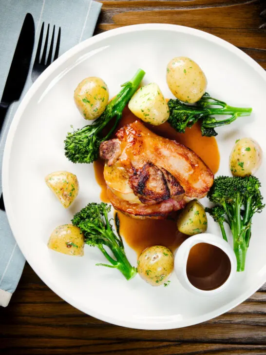 Overhead baked apple and bacon stuffed pork chops, with cider gravy, potatoes and broccoli.