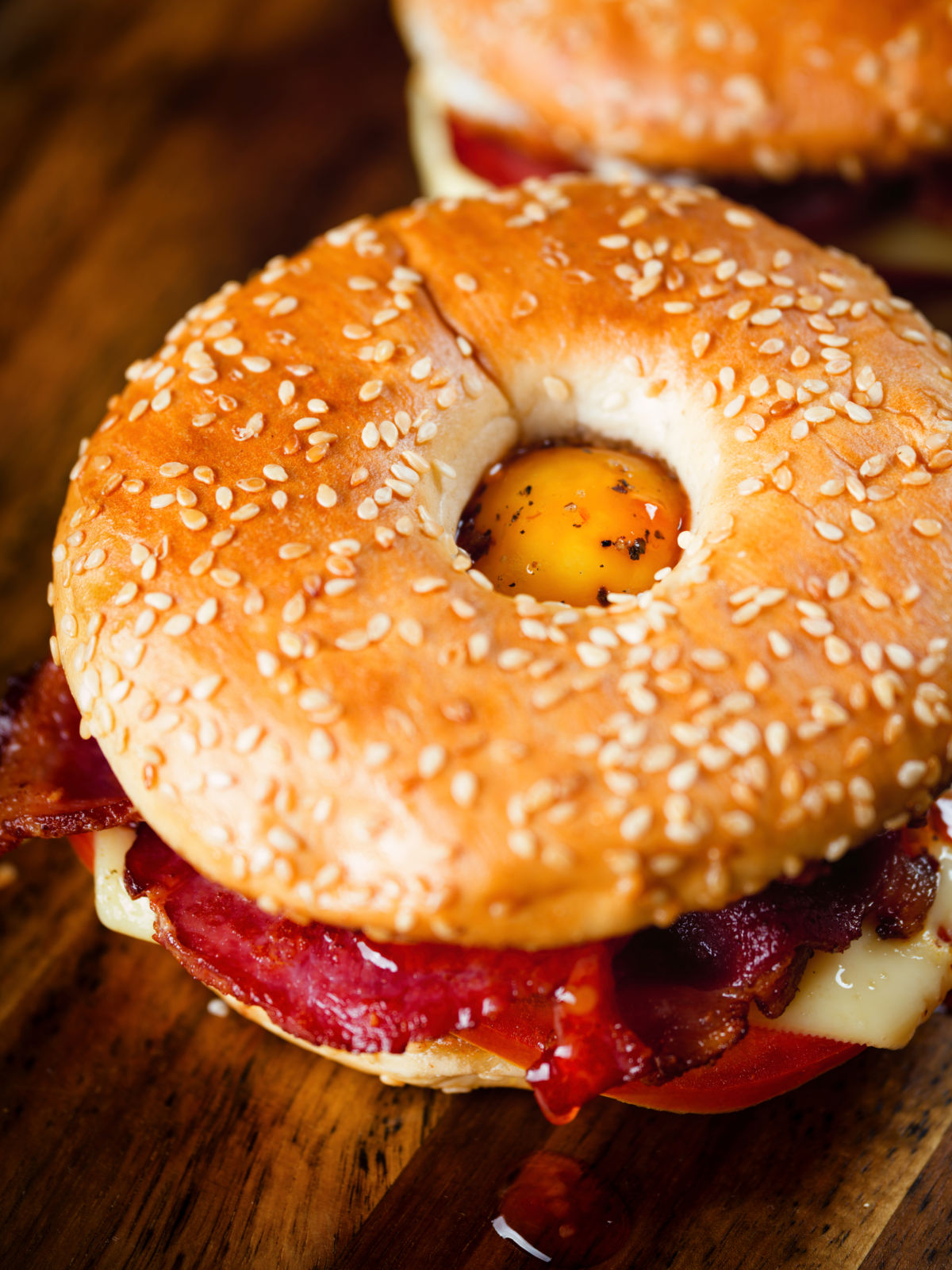 Close-up bacon, egg, tomato and cheese breakfast bagels with sweet chilli sauce.