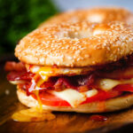 Bacon, egg, tomato and cheese breakfast bagels with a runny yolk and sweet chilli sauce.