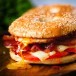 Bacon, egg, tomato and cheese breakfast bagels with a runny yolk and sweet chilli sauce.