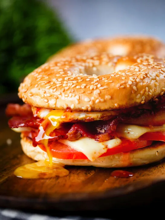 Bacon, egg, tomato and cheese breakfast bagels with a runny yolk and sweet chilli sauce.