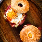 Overhead bacon, egg, tomato and cheese breakfast bagels with sweet chilli sauce.