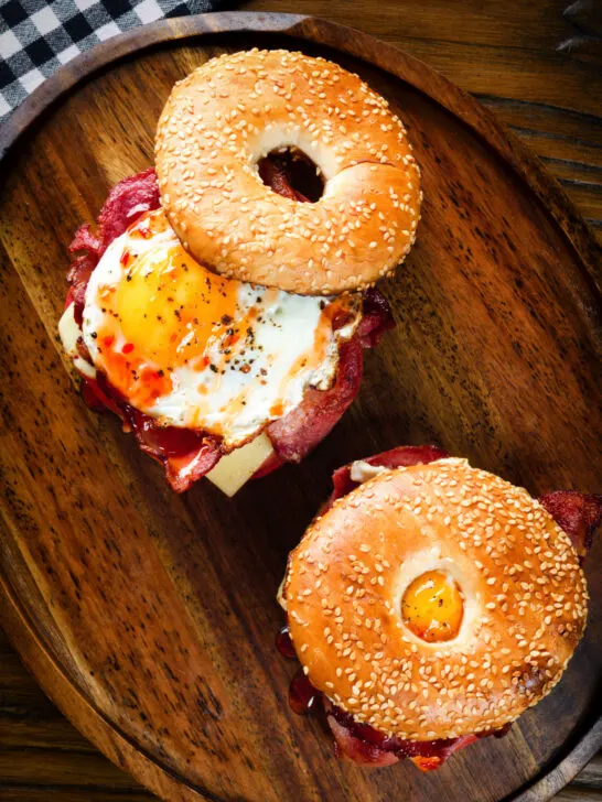 Overhead bacon, egg, tomato and cheese breakfast bagels with sweet chilli sauce.