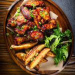 Overhead Chinese chicken wings with spare rib inspired glaze served with potato wedges.