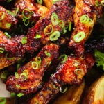 Overhead close-up Chinese chicken wings with spare rib inspired glaze served with potato wedges.