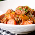 Close-up Filipino pork menudo with liver, hotdog sausages, potatoes and carrots.