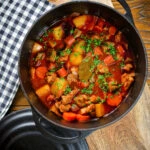 Overhead Filipino pork menudo with liver, hotdog sausages, potatoes and carrots in its cooking pot.