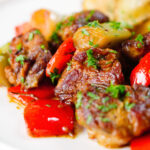 Close-up Greek pork tigania with peppers and leeks, served with watercress and potato wedges.