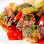 Close-up Greek pork tigania with peppers and leeks, served with watercress and potato wedges.