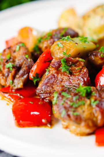 Close-up Greek pork tigania with peppers and leeks, served with watercress and potato wedges.