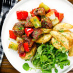 Overhead Greek pork tigania with peppers and leeks, served with watercress and potato wedges.