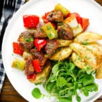 Overhead Greek pork tigania with peppers and leeks, served with watercress and potato wedges.