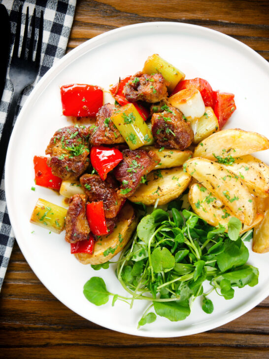 Overhead Greek pork tigania with peppers and leeks, served with watercress and potato wedges.