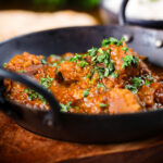 Close-up Indian (Goan) inspired pork vindaloo curry served with rice and naan bread.