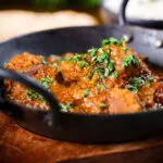 Close-up Indian (Goan) inspired pork vindaloo curry served with rice and naan bread.