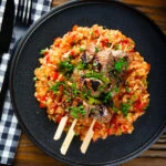 Overhead Portuguese beef espetada skewers served with tomato rice and parsley.
