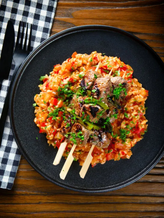 Overhead Portuguese beef espetada skewers served with tomato rice and parsley.