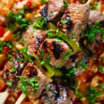 Overhead close-up Portuguese beef espetada skewers served with tomato rice and parsley.