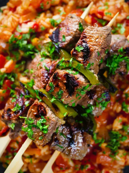 Overhead close-up Portuguese beef espetada skewers served with tomato rice and parsley.