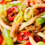 Close-up spicy stir fried sweet chilli chicken udon noodles with peppers.