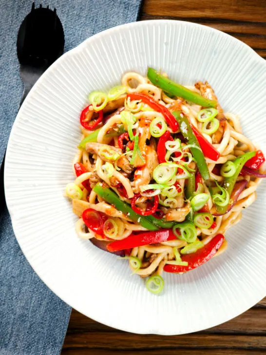 Overhead spicy stir fried sweet chilli chicken udon noodles with peppers.