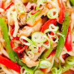 Overhead close-up spicy stir fried sweet chilli chicken udon noodles with peppers.