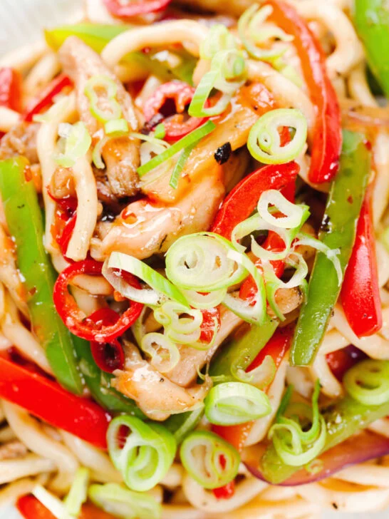 Overhead close-up spicy stir fried sweet chilli chicken udon noodles with peppers.