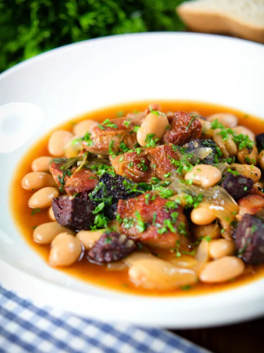 Pork and bean stew with black pudding and sage served in a white bowl.