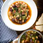 Overhead pork and bean stew with black pudding and sage served with bread.