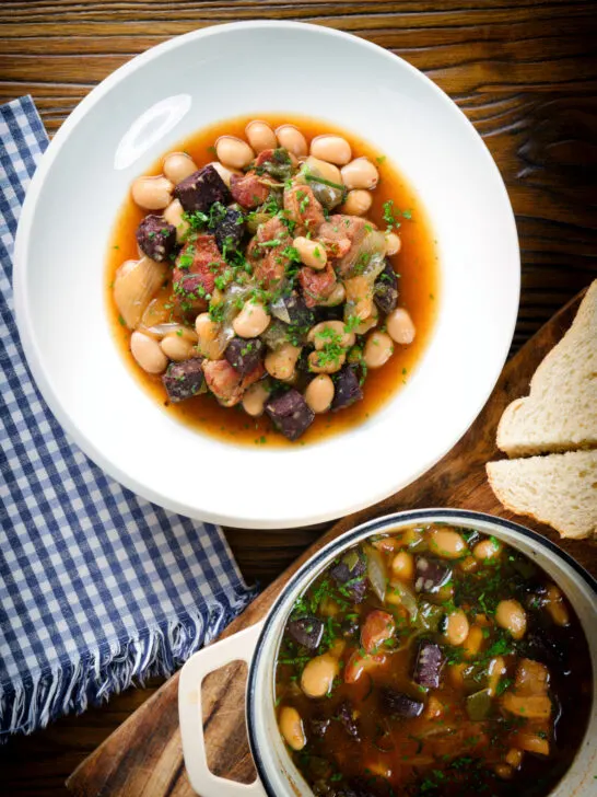 Overhead pork and bean stew with black pudding and sage served with bread.