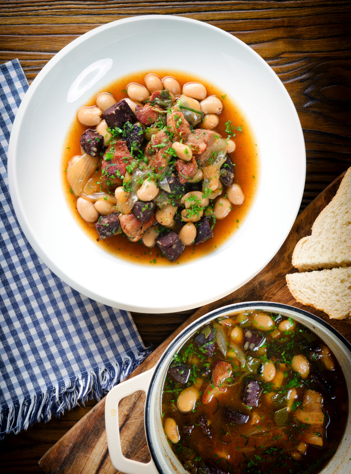 Overhead pork and bean stew with black pudding and sage served with bread.
