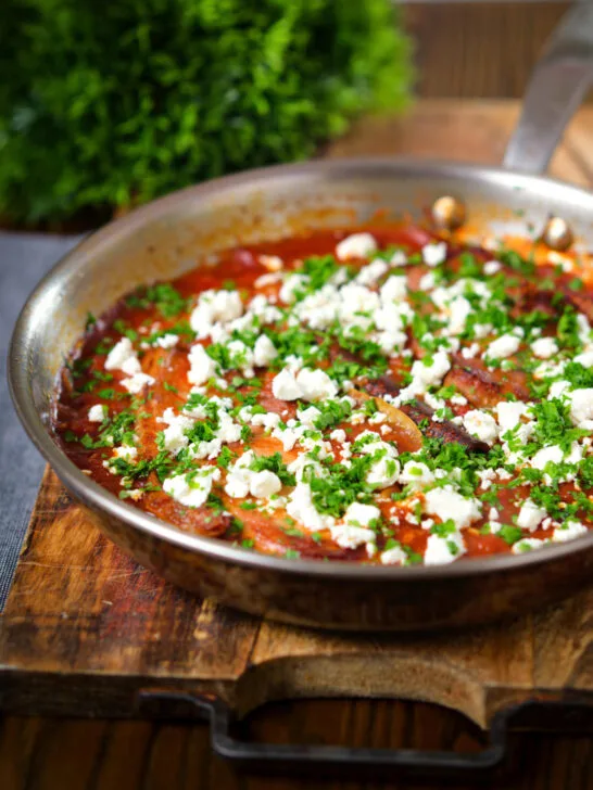 Baked pork chops with tomato orzo, feta cheese and parsley, in its pan.