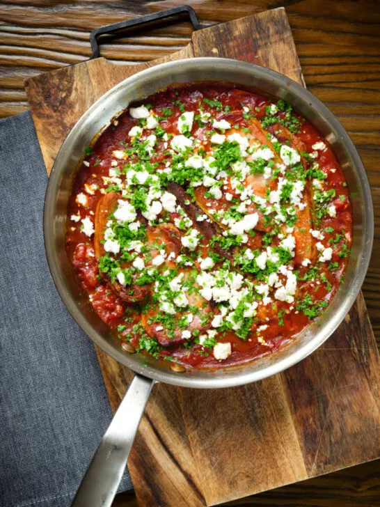 Overhead baked pork chops with tomato orzo, feta cheese and parsley, in its pan.