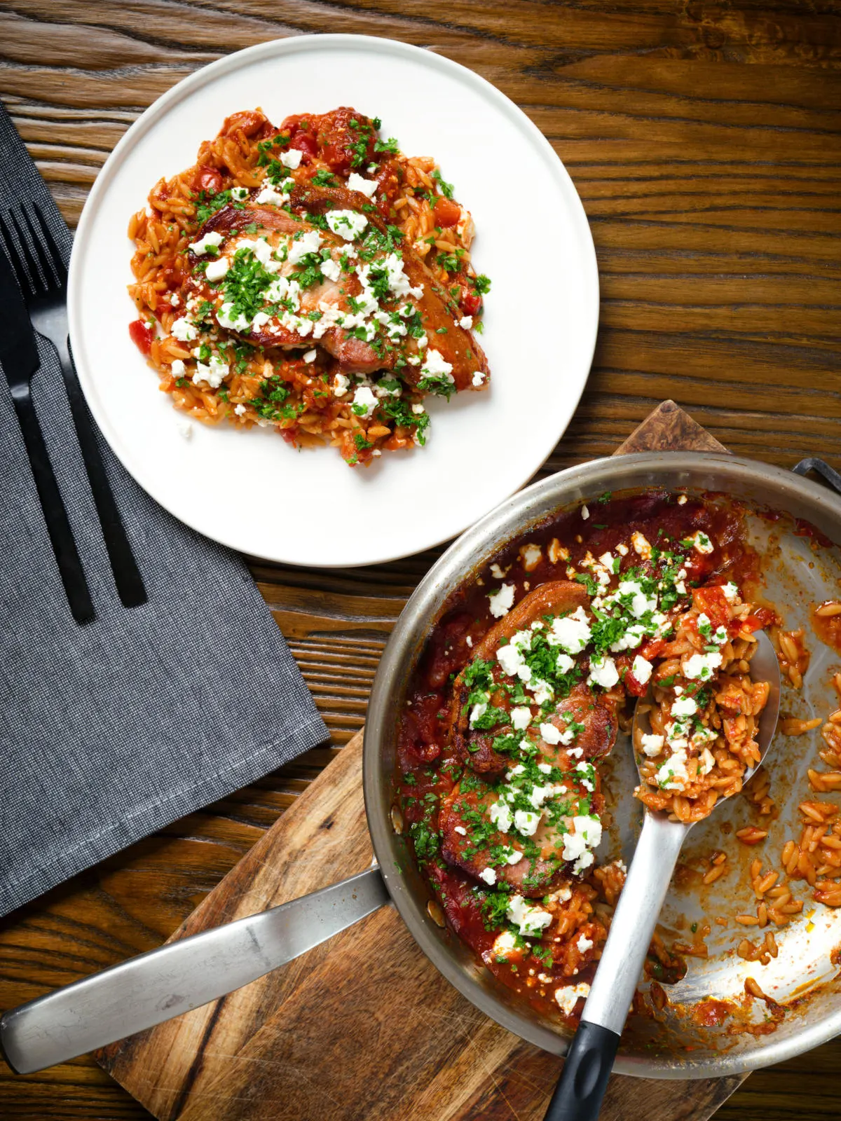 Overhead baked pork chops with tomato orzo, feta cheese and parsley.