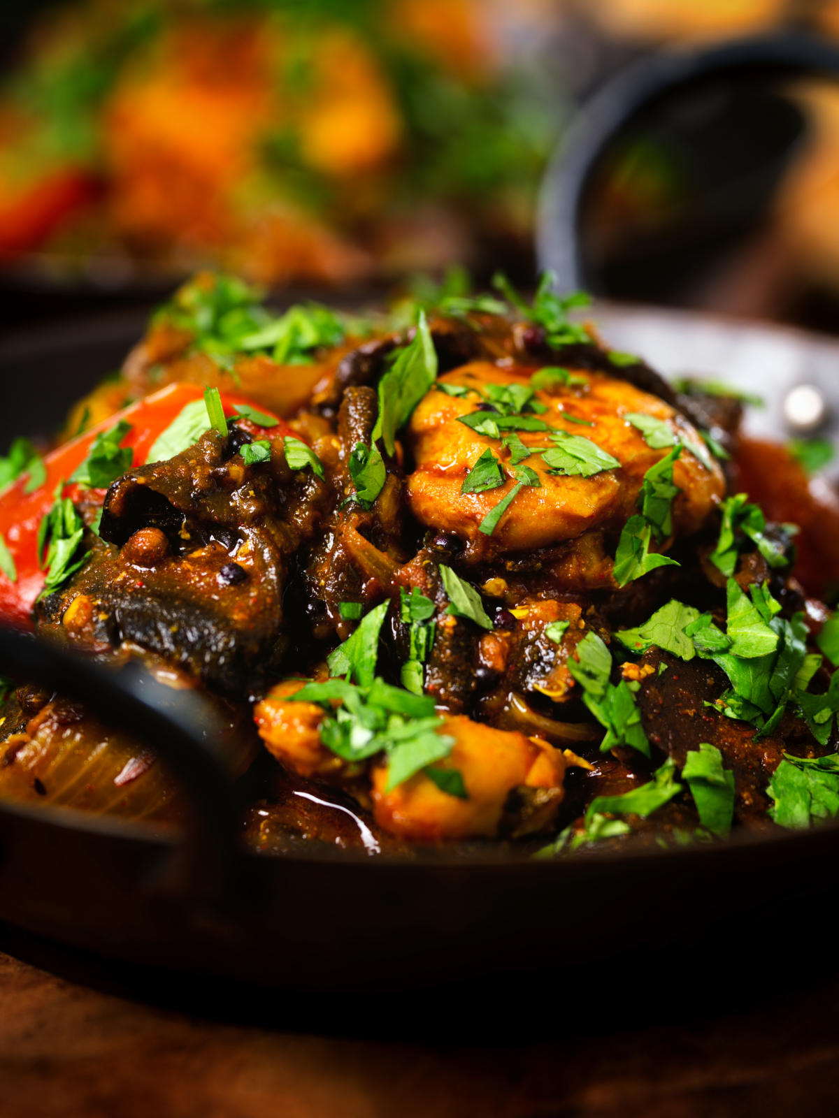 Close-up Indian-influenced chicken, mushroom and tomato curry served in a karai.