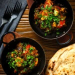 Overhead Indian-influenced chicken, mushroom and tomato curry served with a naan bread.