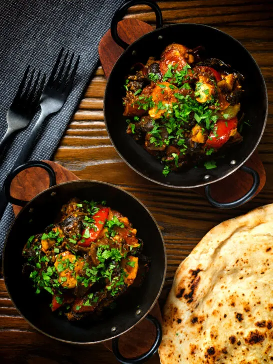 Overhead Indian-influenced chicken, mushroom and tomato curry served with a naan bread.