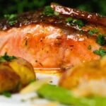 Close-up orange and marmalade glazed salmon with new potatoes and green beans.