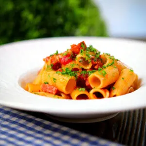 Chorizo sausage and bacon pasta (Rigatoni) in a tomato sauce garnished with fresh parsley.
