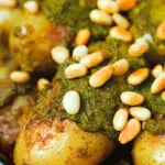 Close-up brown butter and basil pesto potatoes garnished with pine nuts.