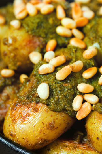Close-up brown butter and basil pesto potatoes garnished with pine nuts.